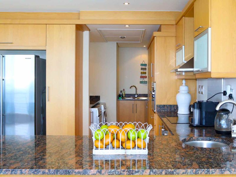 A functional kitchen featuring light wood cabinetry, granite countertops, a breakfast bar, and a separate scullery area with additional sink and laundry space.