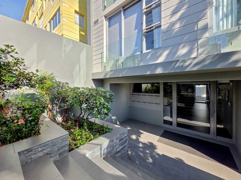 Modern apartment building entrance featuring a glass-fronted door, stone-clad planter box, and sleek tiled flooring in a well-maintained exterior setting.