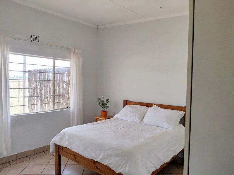 A simple bedroom featuring tiled flooring, a window with security bars, and a built-in cupboard.