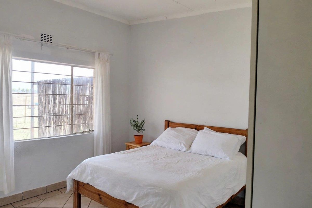 A simple bedroom featuring tiled flooring, a window with security bars, and a built-in cupboard.
