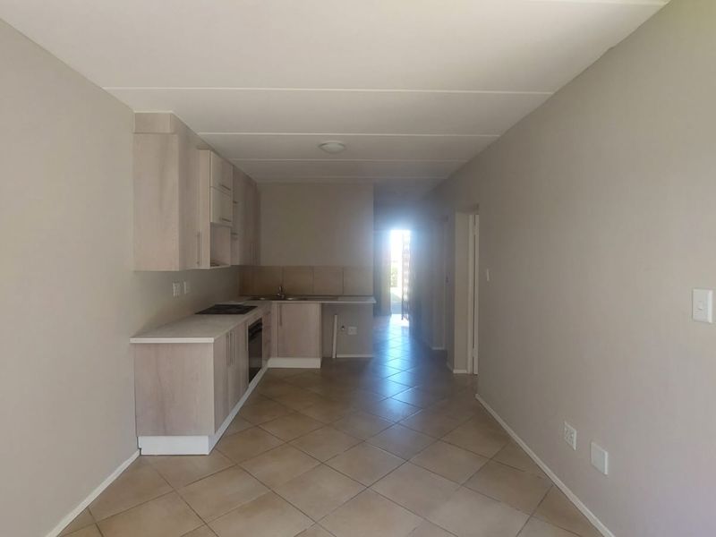 An open-plan kitchen and living area featuring neutral cabinetry, tiled flooring, and built-in cooking appliances in a clean, vacant space.