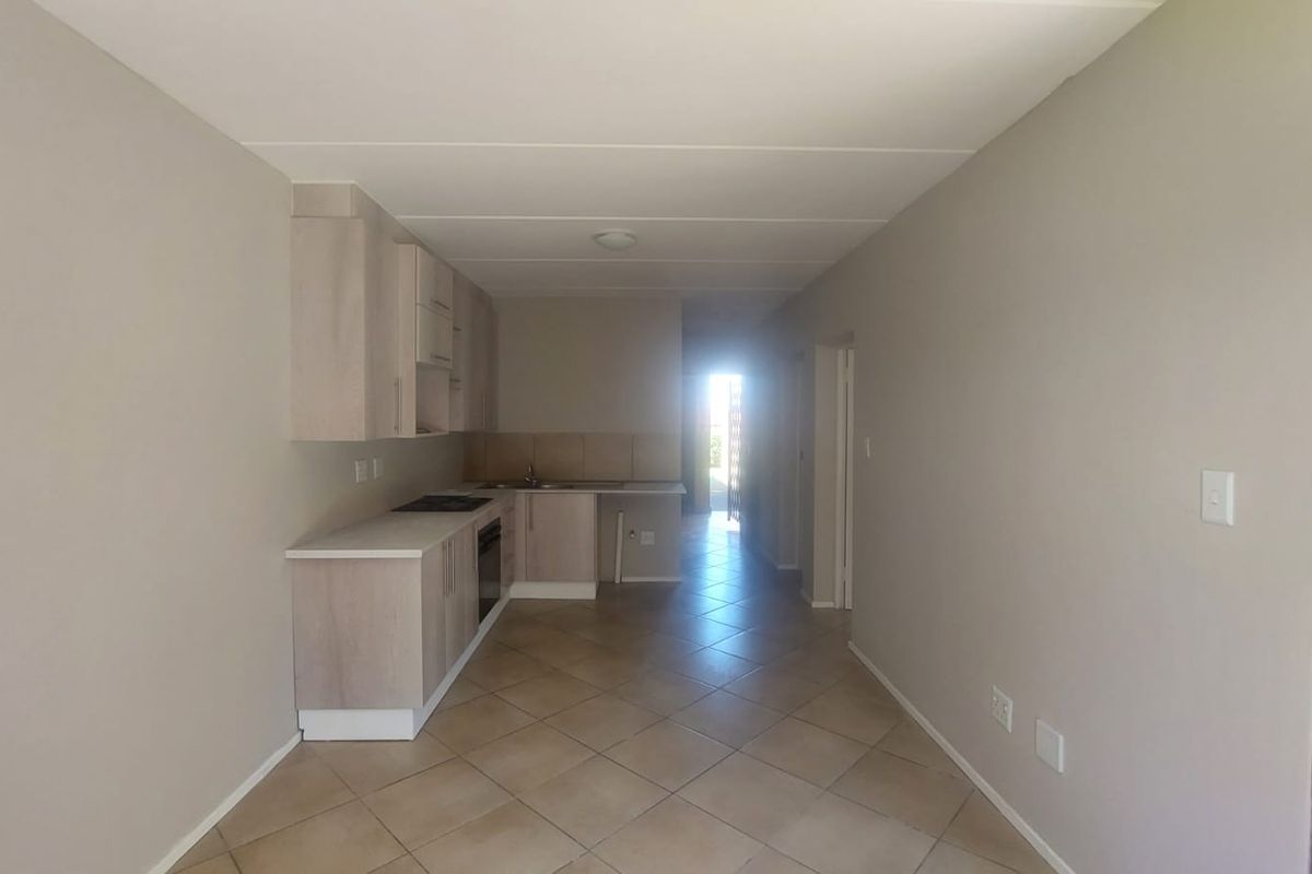 An open-plan kitchen and living area featuring neutral cabinetry, tiled flooring, and built-in cooking appliances in a clean, vacant space.