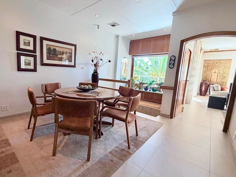 A bright dining area featuring tiled flooring, recessed lighting, and built-in cabinetry, with an open archway leading to an adjacent living space.