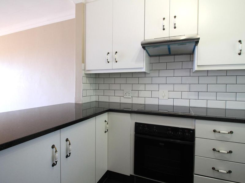 A clean, modern kitchen featuring white cabinetry, black granite countertops, a subway tile backsplash, and integrated electric cooking appliances.
