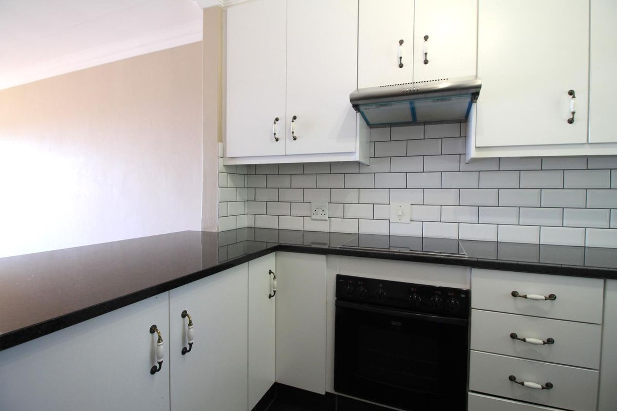 A clean, modern kitchen featuring white cabinetry, black granite countertops, a subway tile backsplash, and integrated electric cooking appliances.