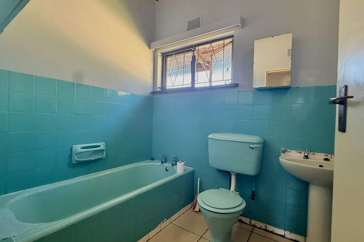 A dated bathroom featuring original blue sanitaryware, tiled walls, and a pedestal sink, offering significant potential for a modern renovation.