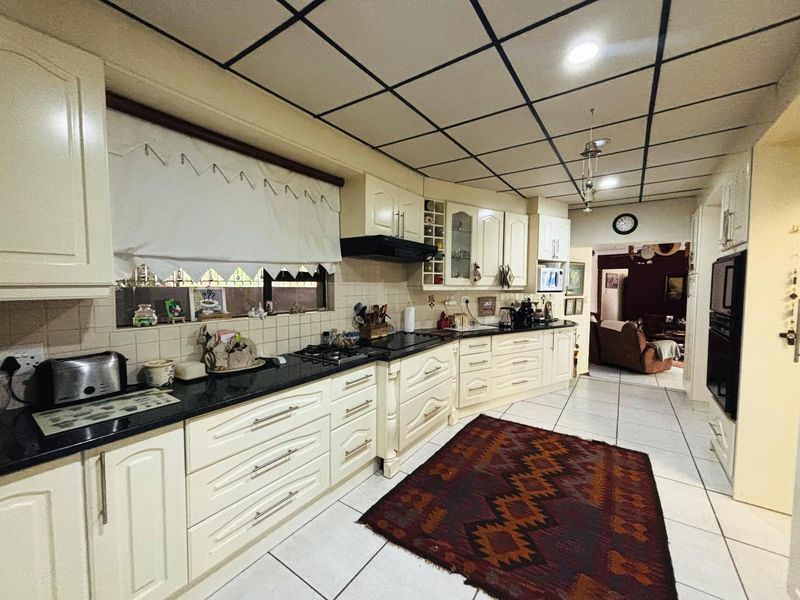 Spacious kitchen featuring cream cabinetry, granite countertops, built-in appliances, and tiled flooring, offering a functional layout with potential for modern updates.