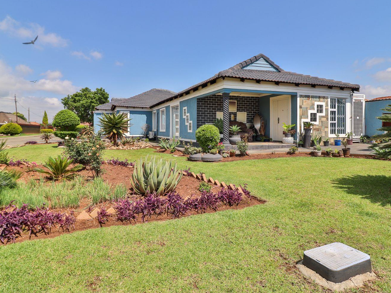 A well-maintained single-story house featuring a tiled roof, stone-clad accents, a covered front patio, and a neatly landscaped front garden.