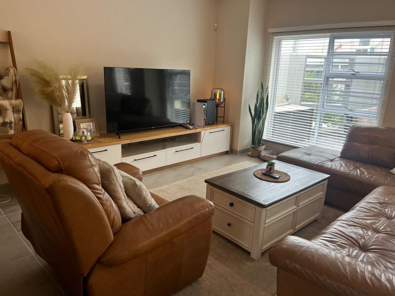 A comfortable living room featuring tiled flooring and a large window with venetian blinds, providing ample natural light.