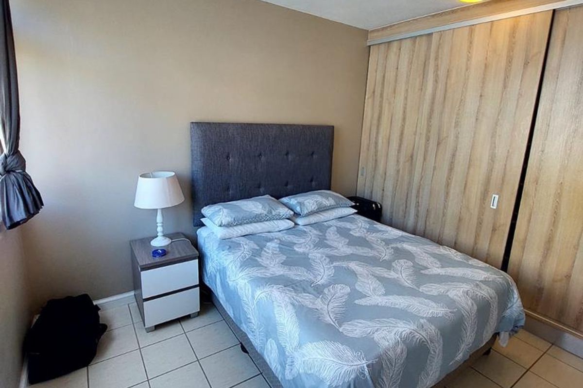 A bedroom featuring tiled flooring, built-in wooden sliding door cupboards, and two flush-mount ceiling lights.