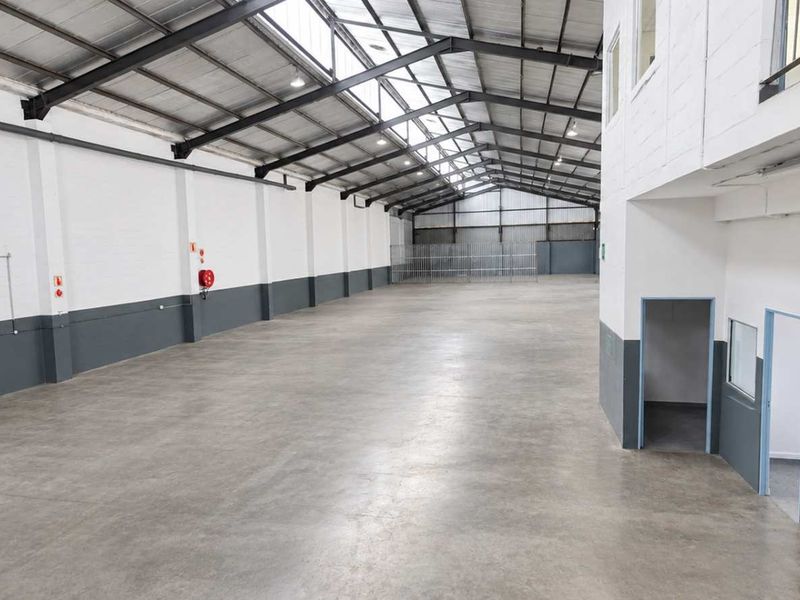 Spacious industrial warehouse unit featuring high ceilings with exposed steel trusses, concrete flooring, mezzanine level, and integrated security gates.