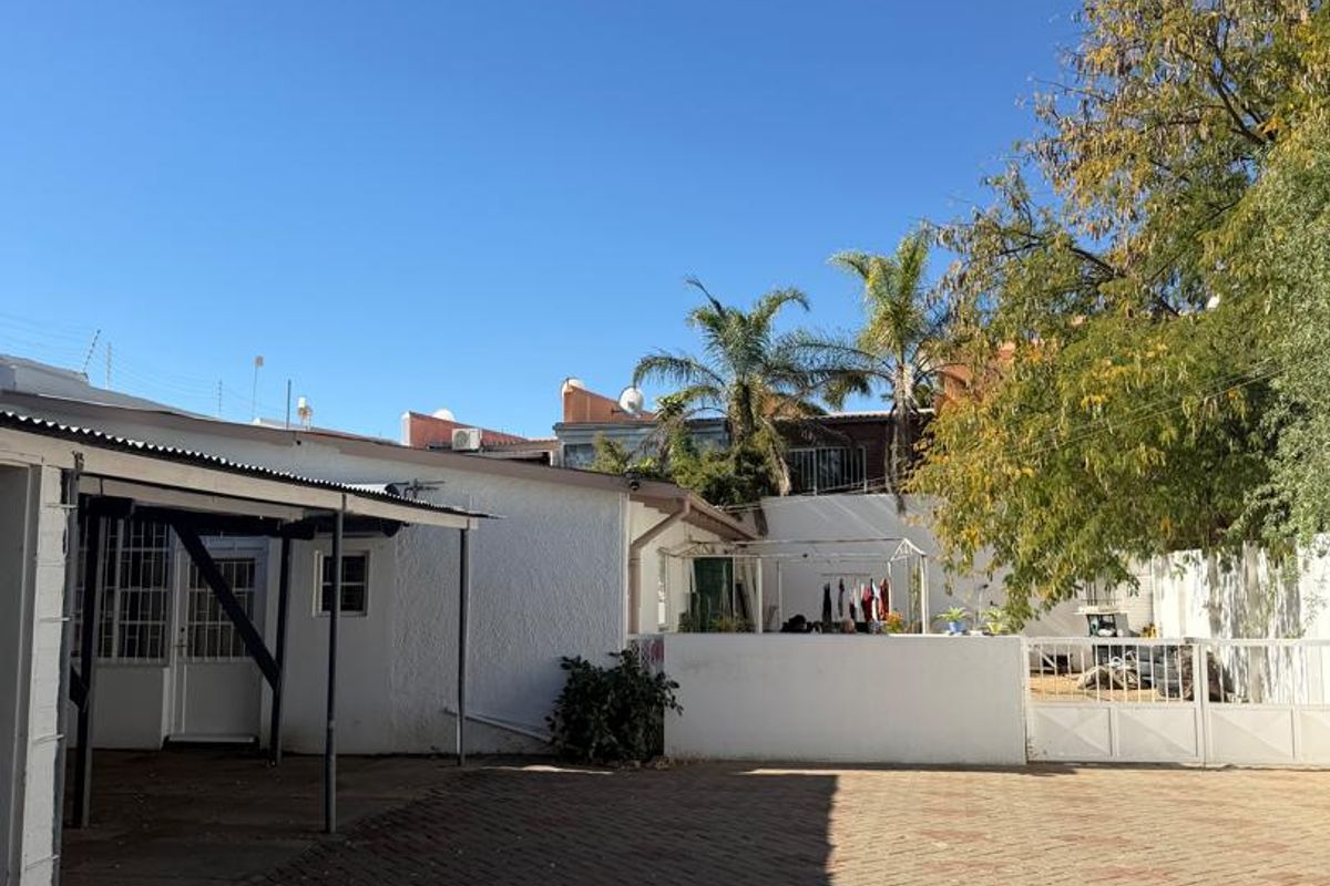 A paved rear courtyard area featuring a covered patio space, secure boundary walls, and gated access.