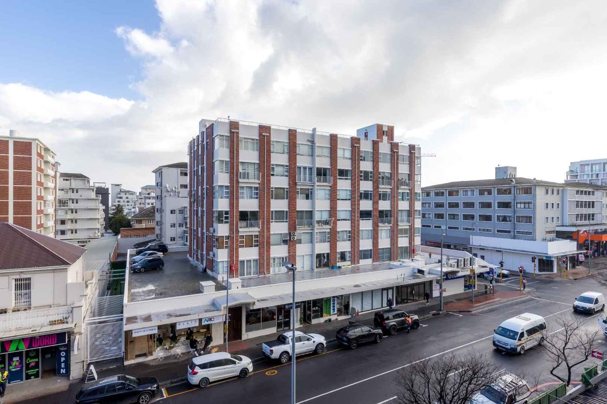 An elevated aerial view of a multi-story apartment building featuring a brick facade, balconies, and ground-level commercial retail spaces.