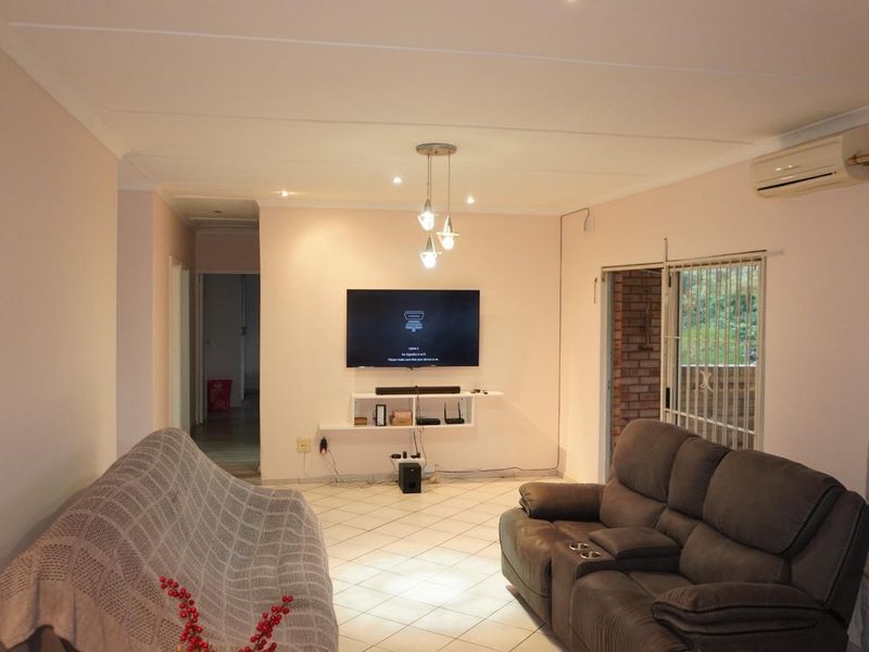 A comfortable living room featuring tiled flooring, recessed lighting, an air conditioning unit, and direct access to an outdoor area through a sliding glass door.
