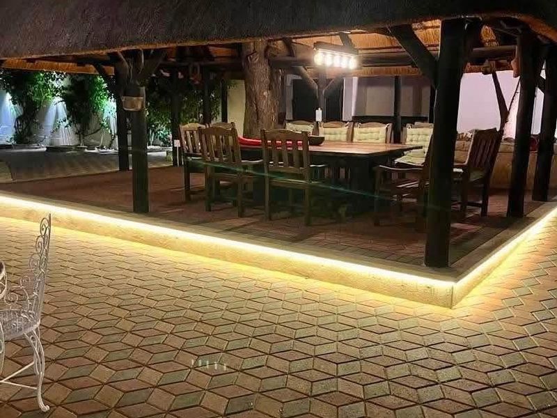 A well-lit outdoor thatched patio area featuring timber support posts and decorative paved flooring, ideal for evening entertainment.