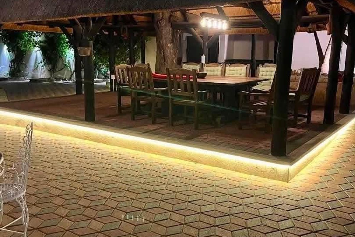 A well-lit outdoor thatched patio area featuring timber support posts and decorative paved flooring, ideal for evening entertainment.