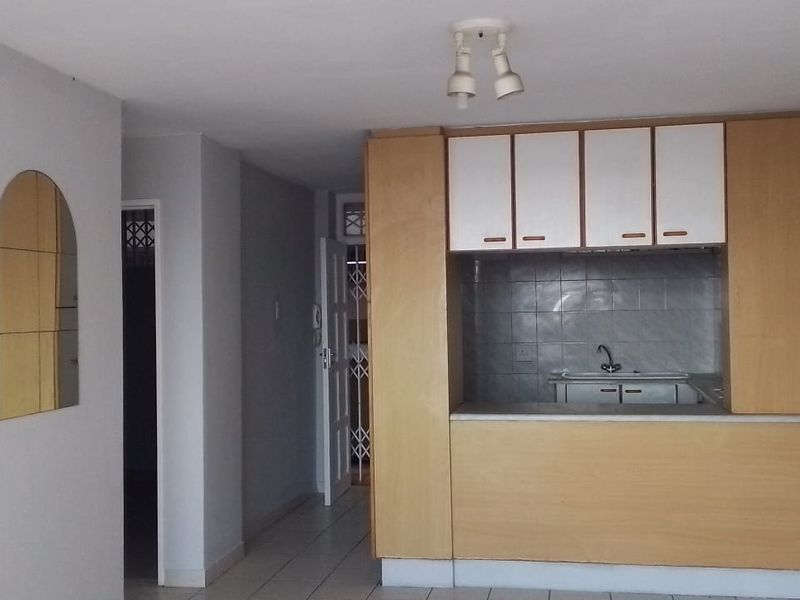 Open plan living area featuring a compact kitchen with built-in cabinetry and tiled flooring throughout.