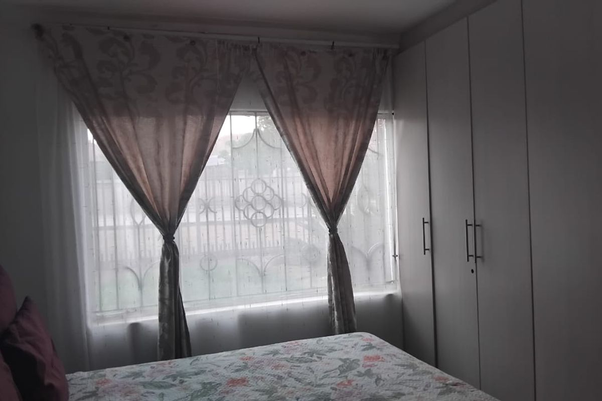 A bedroom featuring built-in floor-to-ceiling wardrobes and a window fitted with security bars.