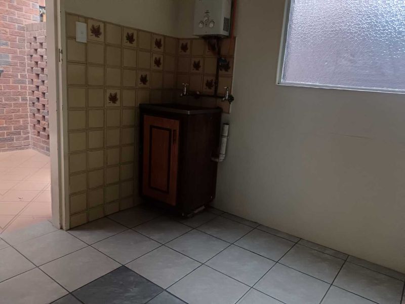 A functional laundry area featuring tiled flooring, a built-in sink with splashback tiles, and a wall-mounted gas geyser.