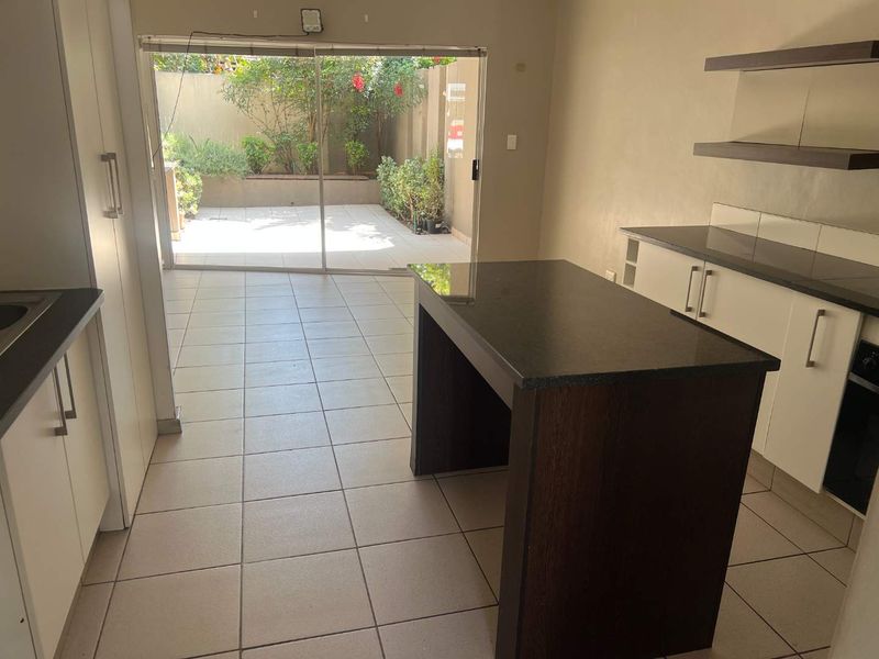 Open plan kitchen area featuring dark granite countertops, white cabinetry, and a central island, with direct access to a paved rear patio.
