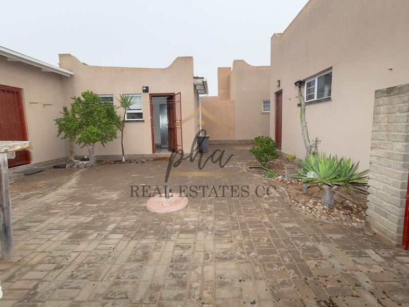 A paved rear courtyard area featuring multiple access points with security gates and surrounding parapet walls, offering a functional outdoor space.