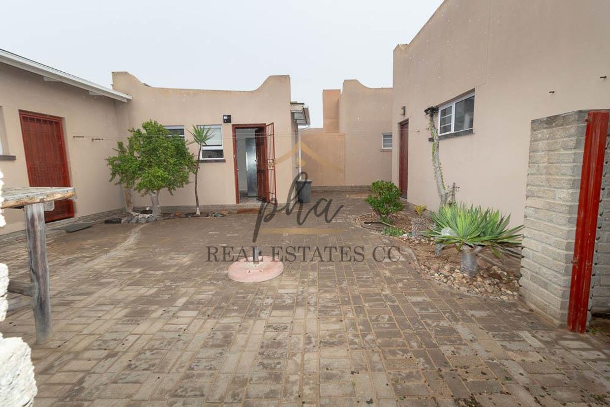A paved rear courtyard area featuring multiple access points with security gates and surrounding parapet walls, offering a functional outdoor space.