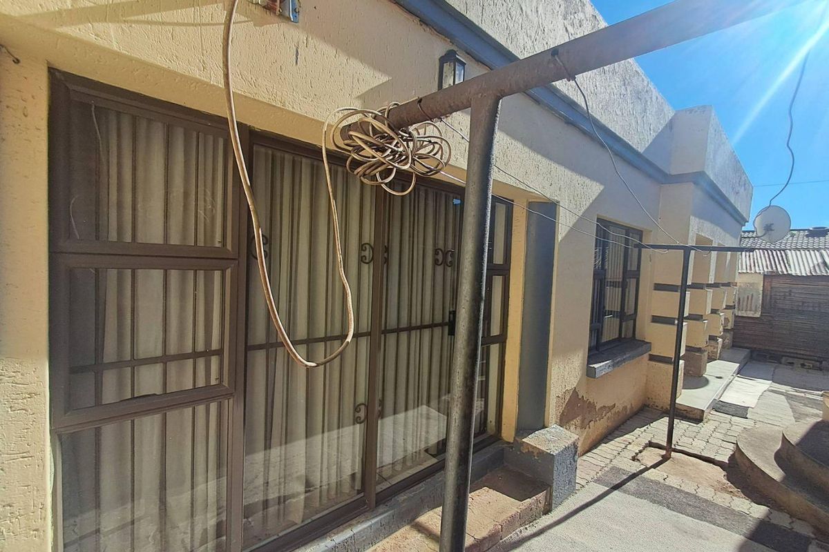 Rear exterior view of the property featuring a paved patio area, sliding glass doors with security bars, and a weathered metal support structure.
