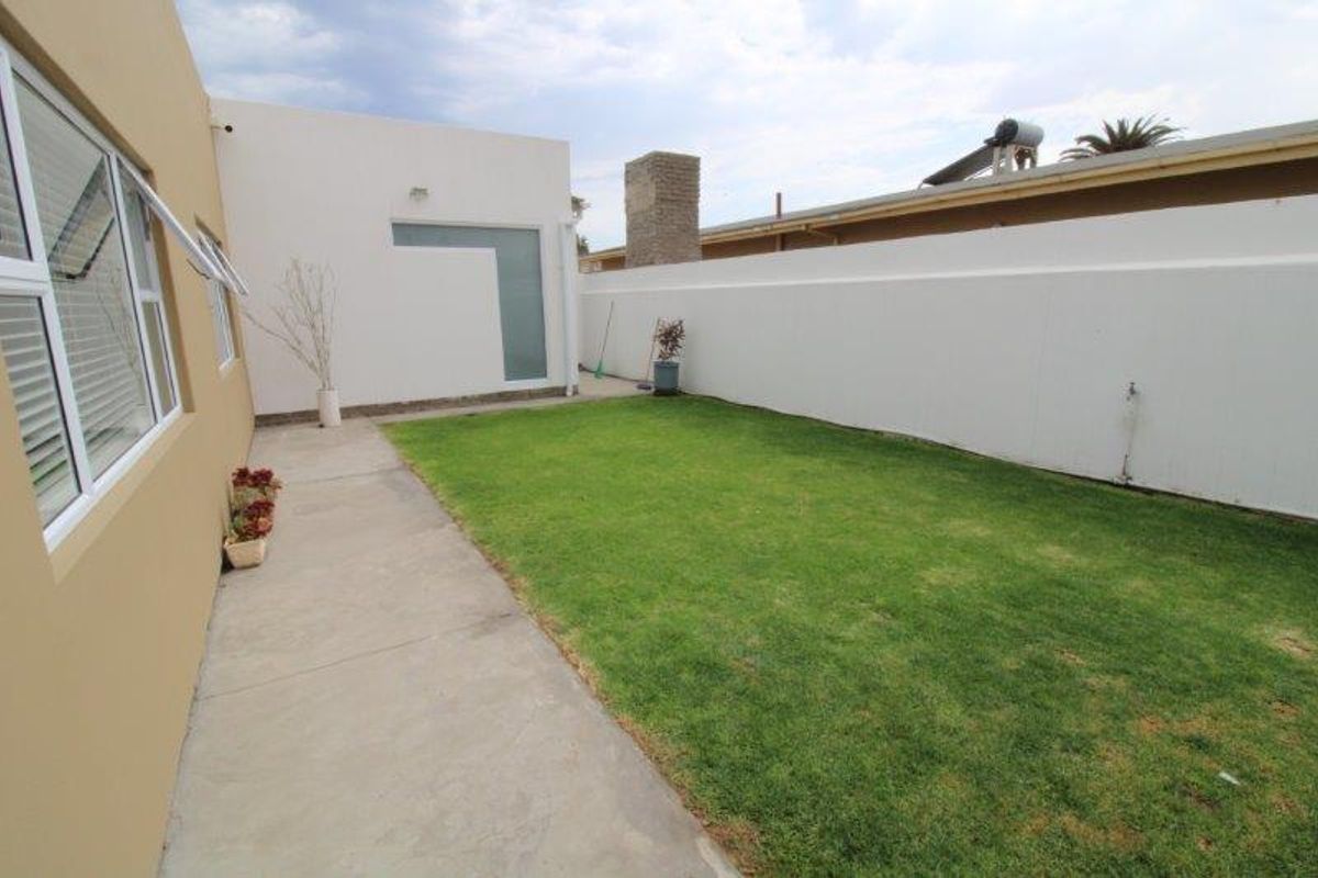 A private rear garden featuring a well-maintained lawn, concrete pathway, and high boundary walls, providing a secure and functional outdoor space.