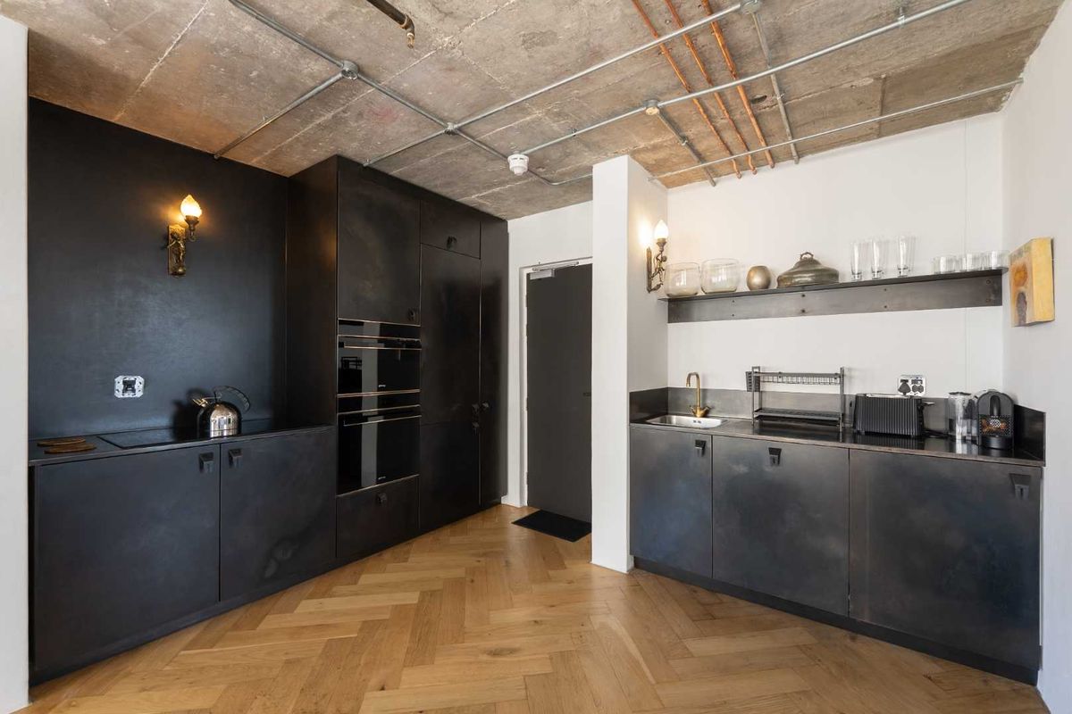 Modern industrial-style kitchen featuring exposed concrete ceilings, herringbone timber flooring, sleek dark cabinetry, and high-end built-in appliances.