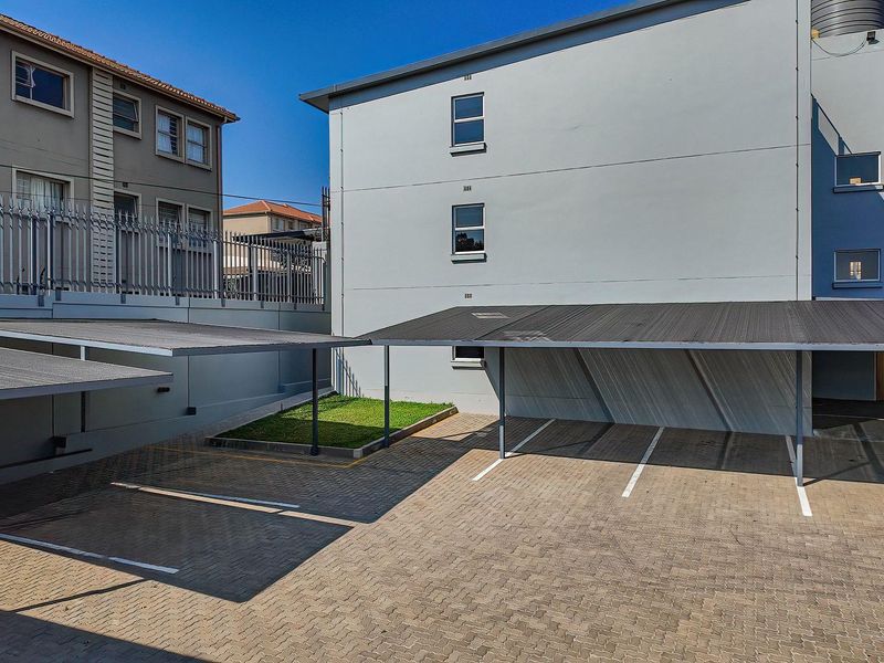 A well-maintained paved parking area featuring covered carports and secure perimeter fencing within the apartment complex grounds.