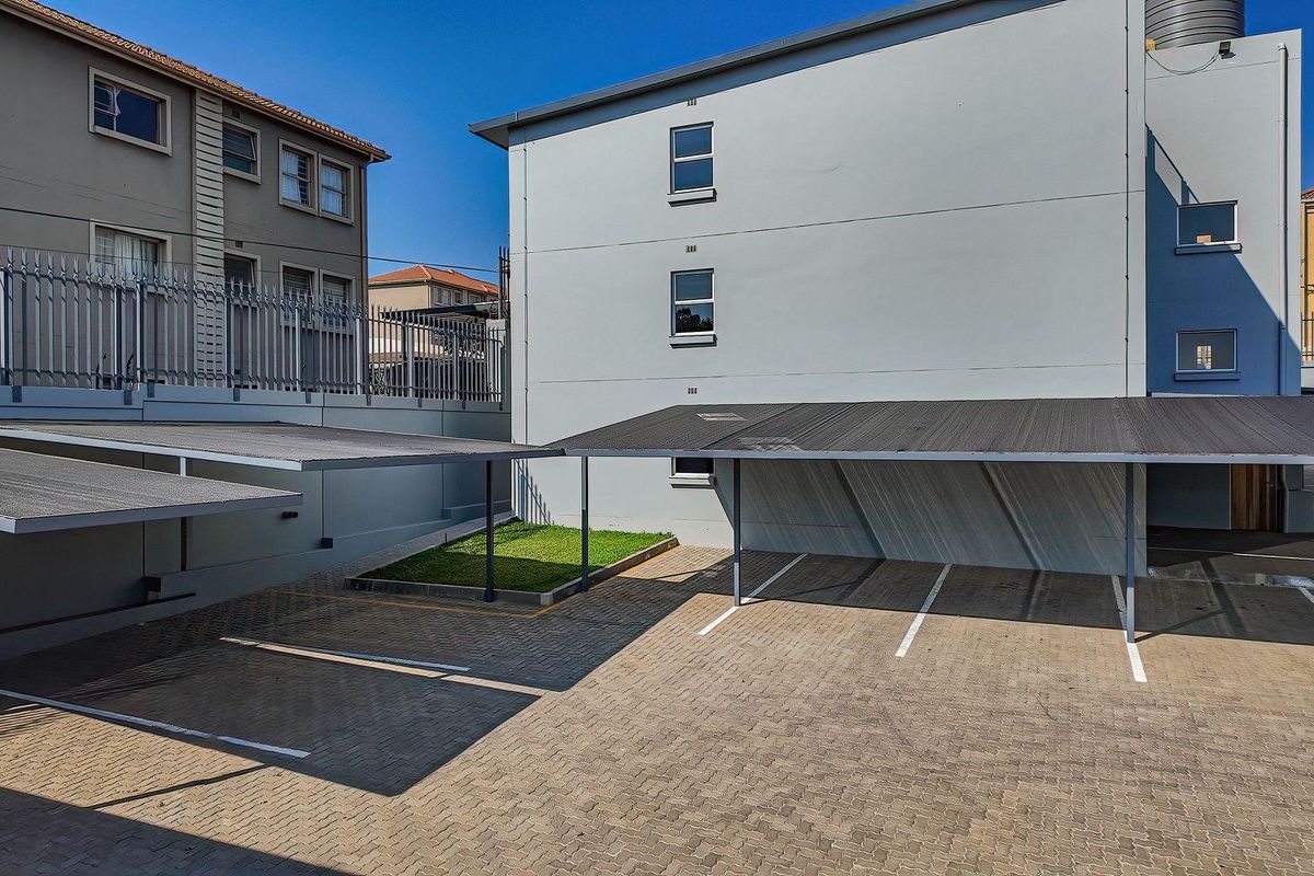 A well-maintained paved parking area featuring covered carports and secure perimeter fencing within the apartment complex grounds.