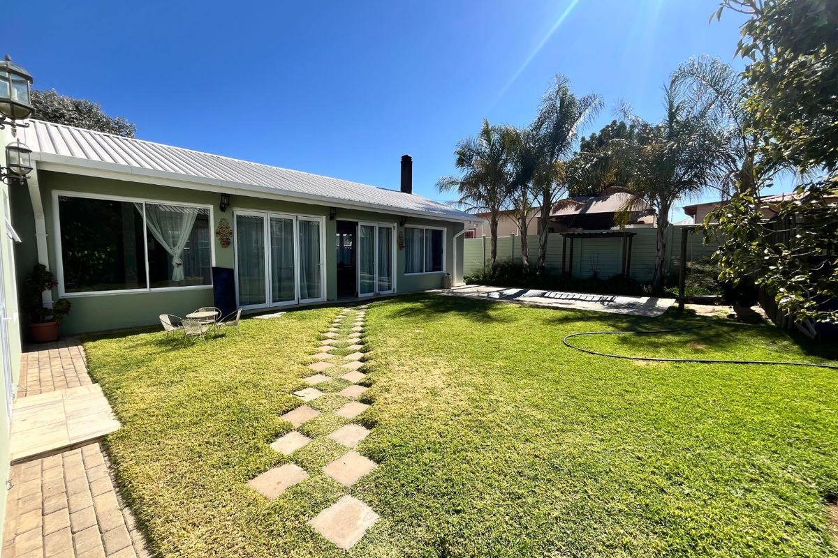 A well-maintained rear garden featuring a lush lawn, stone paver path, and direct access to the home via multiple sliding glass doors.