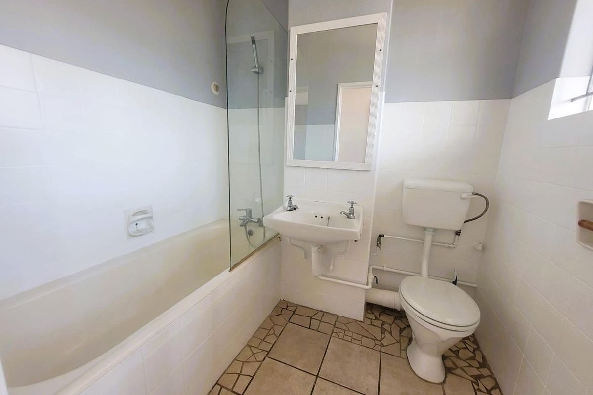 A functional bathroom featuring a bathtub with a glass shower screen, a wall-mounted basin, and a standard toilet with exposed plumbing.