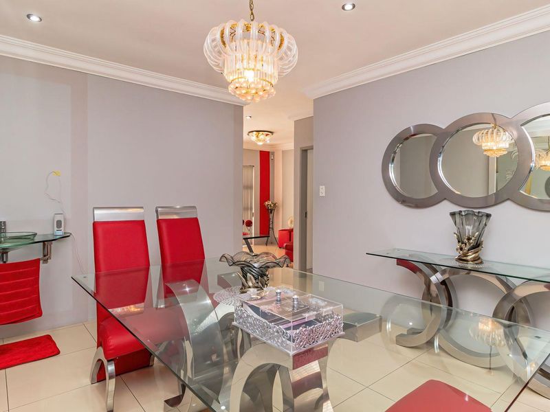 A well-lit dining room featuring tiled flooring, crown molding, and a decorative chandelier, with a unique wall-mounted glass basin integrated into the space.