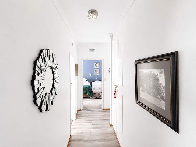 A bright, clean hallway featuring light-toned laminate flooring, built-in storage cupboards, and a neutral color palette leading toward a bedroom.