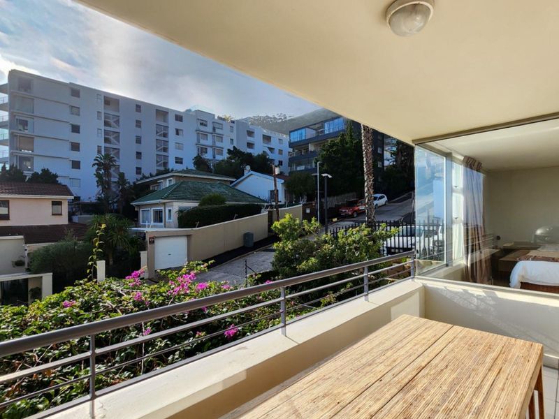 A covered balcony featuring a metal balustrade and views of the surrounding neighborhood and apartment complex.