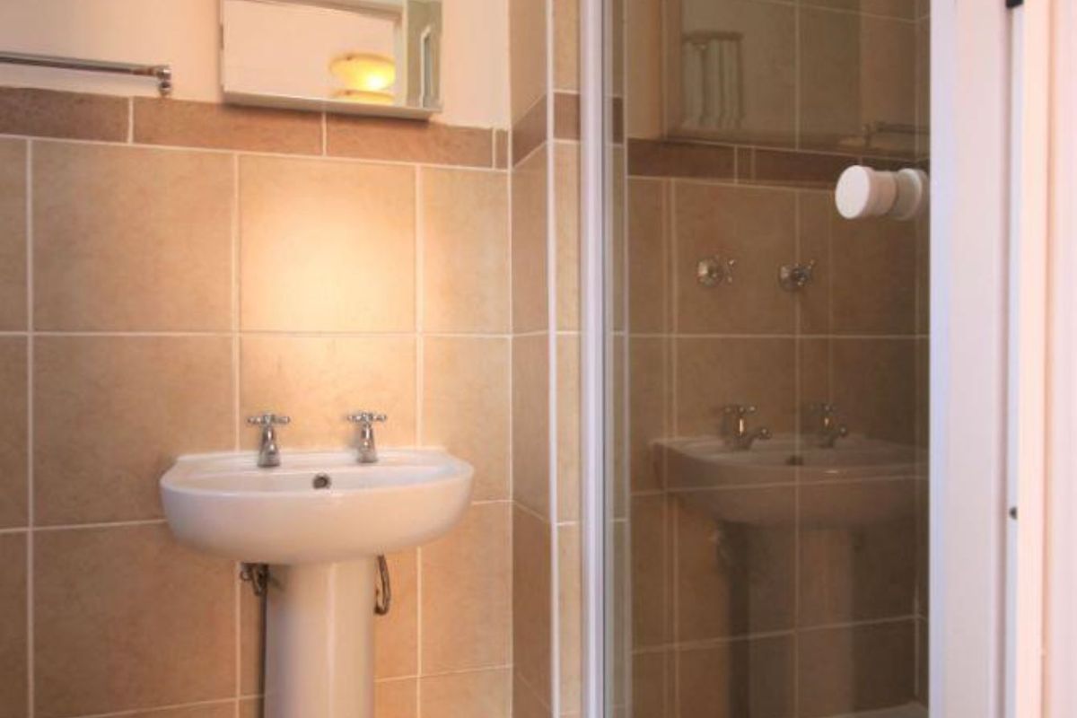 A functional bathroom featuring a pedestal basin, a glass-enclosed shower, and neutral wall and floor tiling.