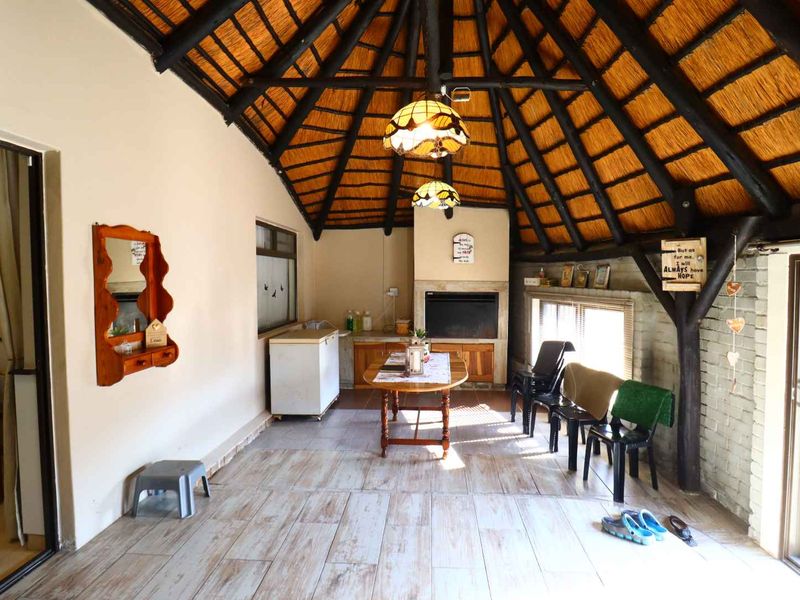 Spacious covered patio featuring a traditional thatched roof with exposed timber beams, a built-in fireplace, and tiled flooring, offering a rustic entertainment space.