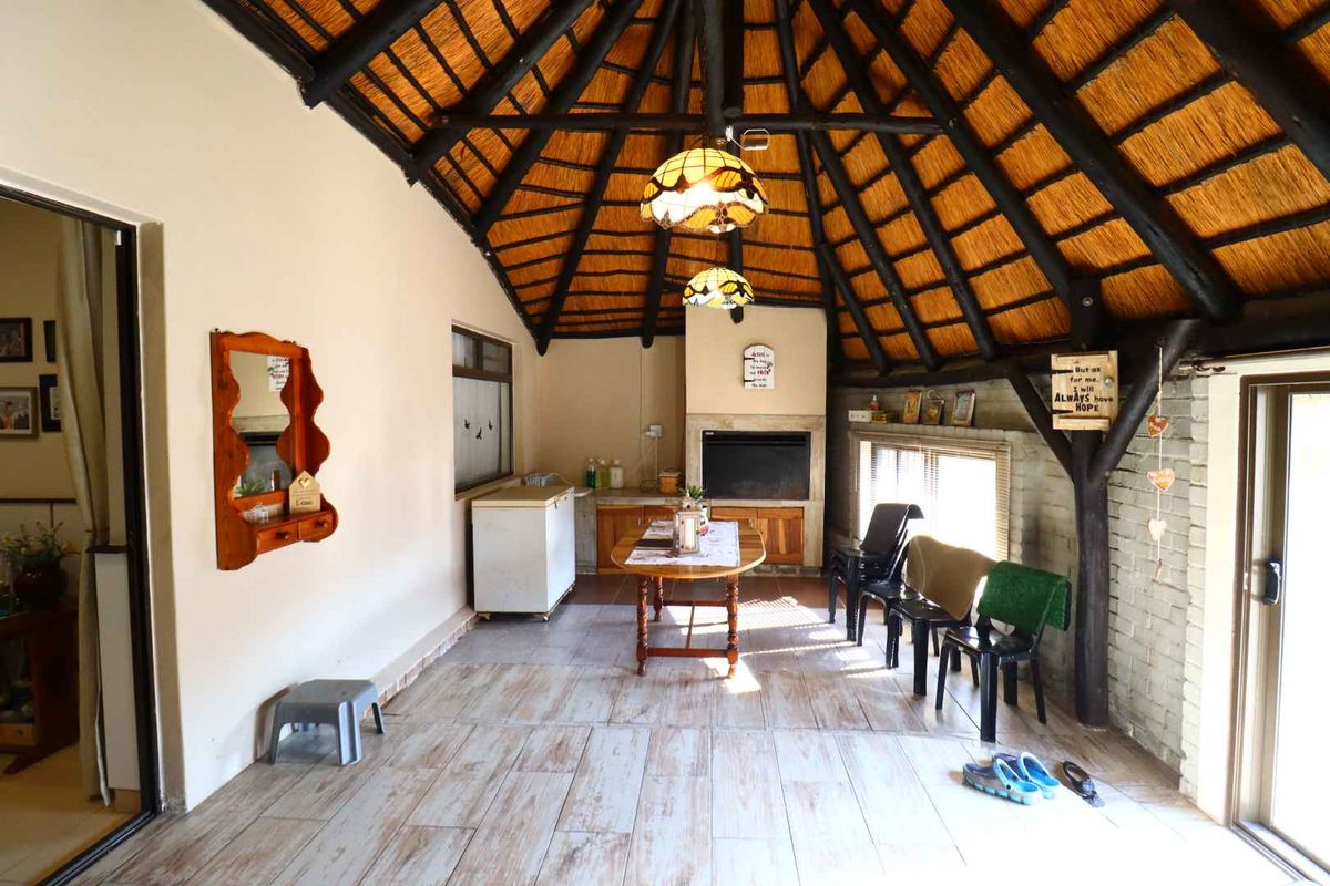 Spacious covered patio featuring a traditional thatched roof with exposed timber beams, a built-in fireplace, and tiled flooring, offering a rustic entertainment space.