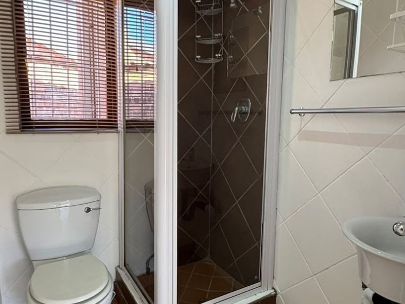 A functional bathroom featuring a corner shower enclosure, pedestal basin, toilet, and tiled finishes throughout.