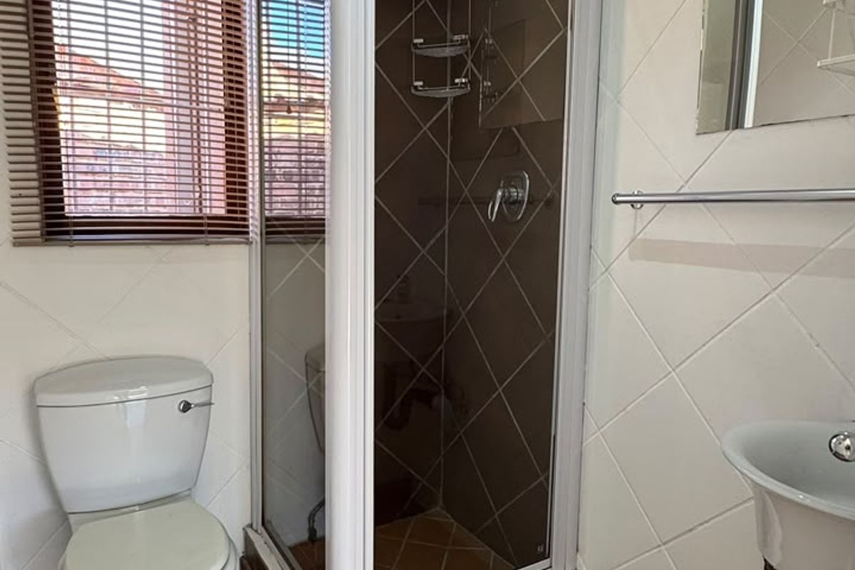 A functional bathroom featuring a corner shower enclosure, pedestal basin, toilet, and tiled finishes throughout.