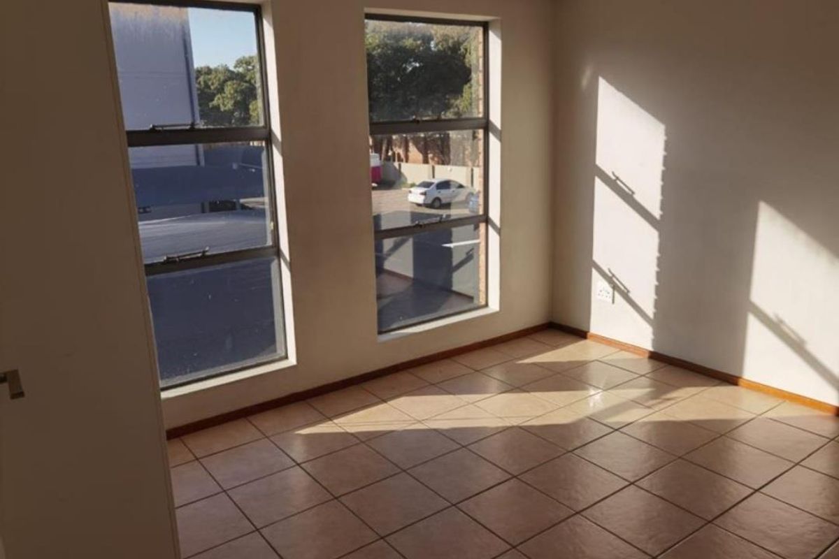A bright, empty bedroom featuring tiled flooring and large windows that provide ample natural light and views of the surrounding area.