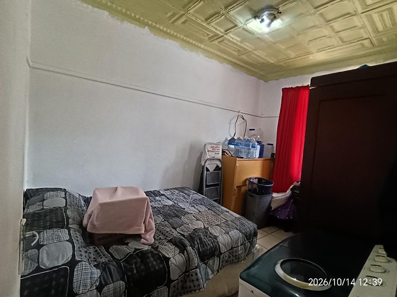 A bedroom featuring a vintage pressed metal ceiling and tiled flooring, currently requiring cosmetic updates and repairs to the wall and ceiling finishes.