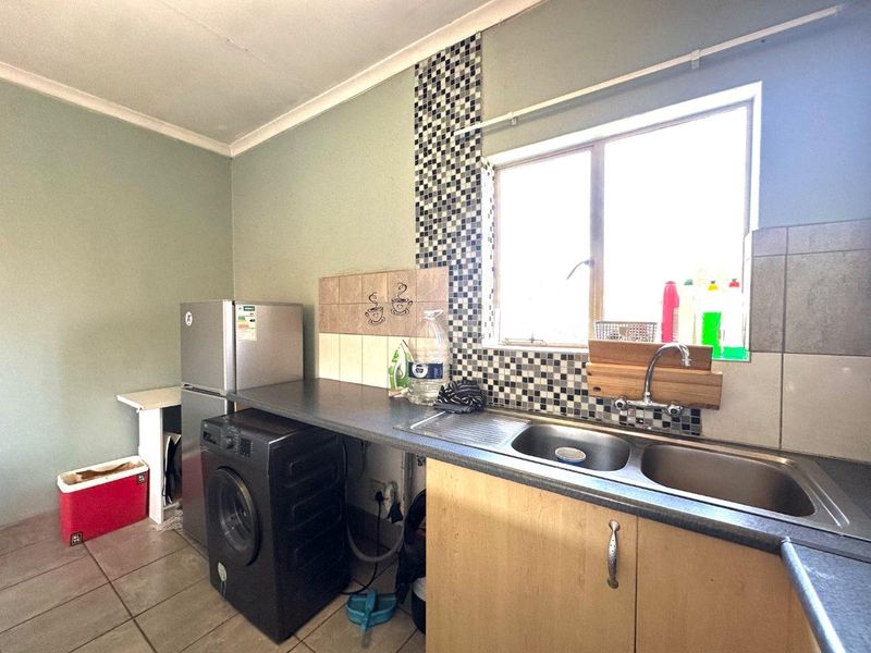 Functional kitchen area featuring a double bowl stainless steel sink, laminate countertops, and tiled splashback with built-in cabinetry.
