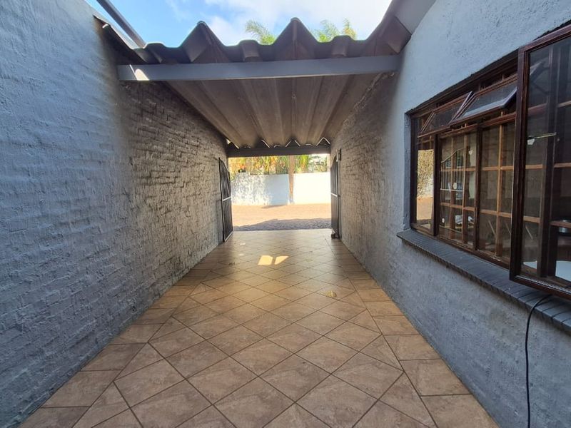 A covered outdoor patio area featuring tiled flooring, brick walls, and timber-framed windows, providing a functional transition space between the interior and exterior.