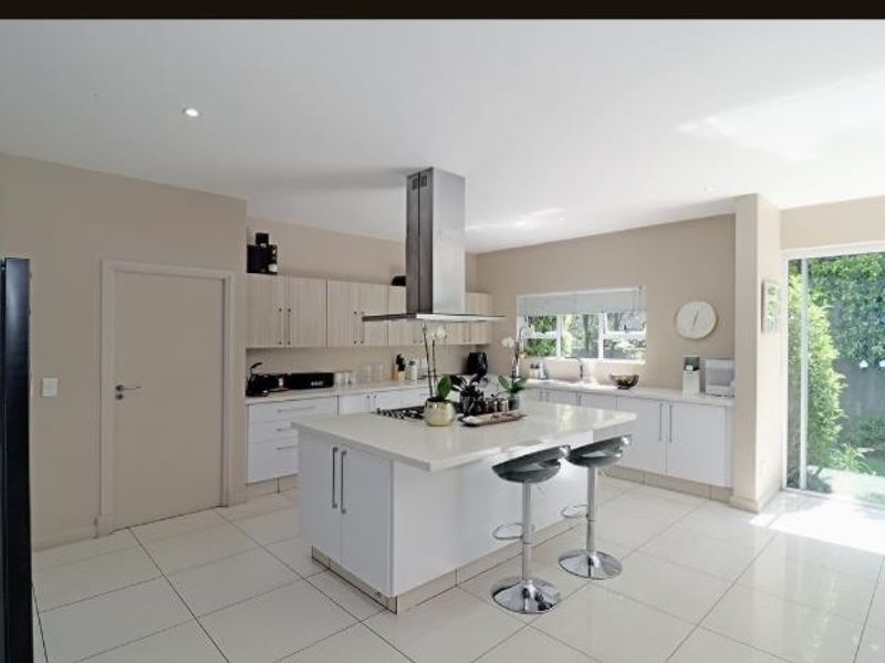 Modern kitchen featuring a central island with stone countertops, stainless steel extractor fan, ample cabinetry, and direct access to the garden through sliding doors.
