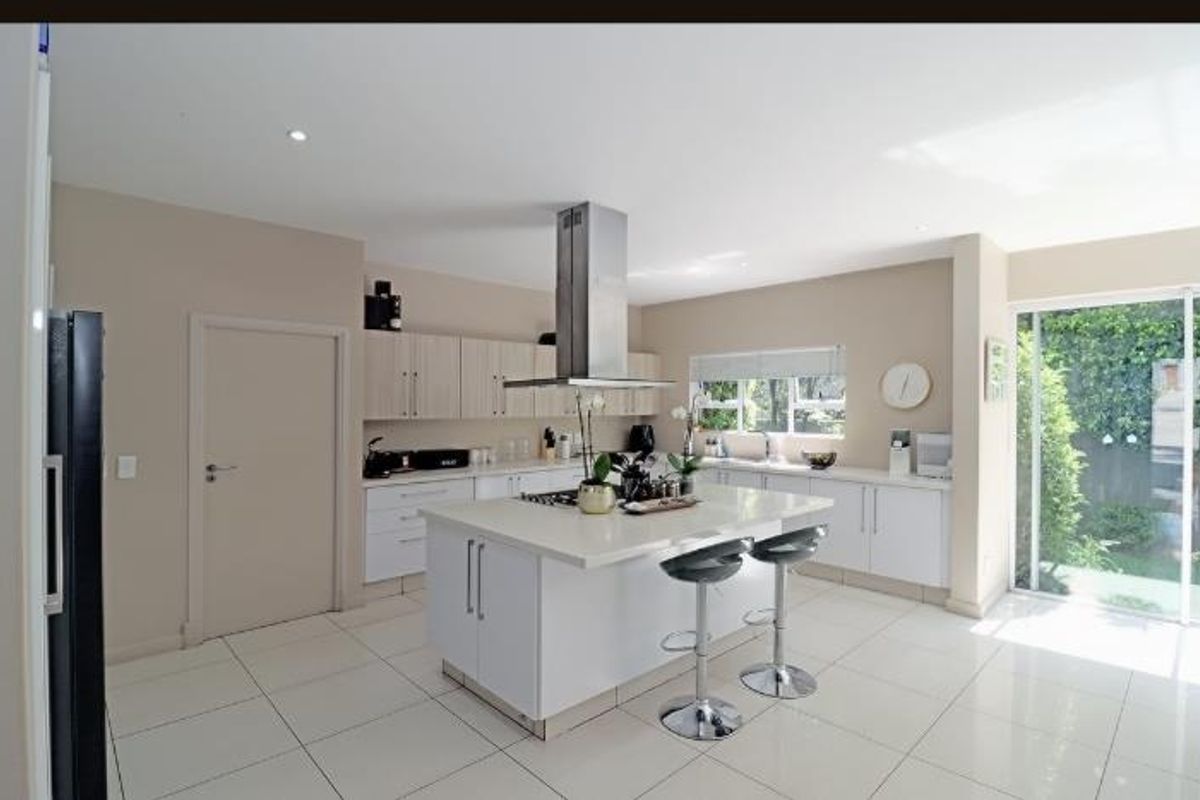 Modern kitchen featuring a central island with stone countertops, stainless steel extractor fan, ample cabinetry, and direct access to the garden through sliding doors.