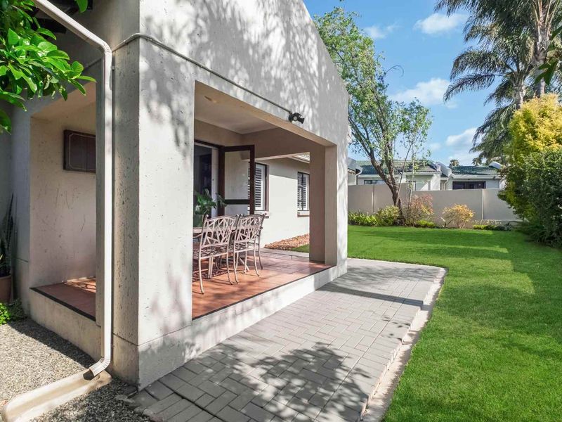 A well-maintained covered patio featuring tiled flooring, leading out to a paved walkway and a neat, landscaped garden area.