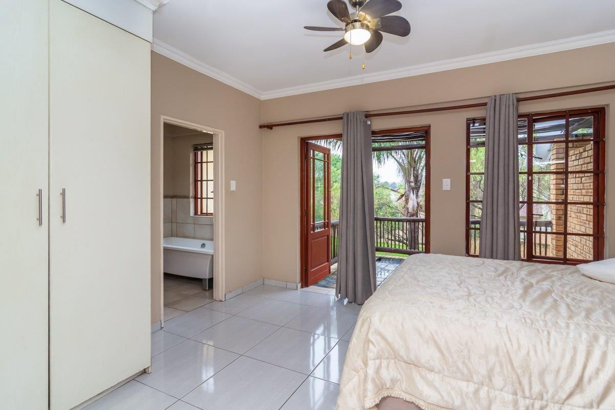 Spacious bedroom featuring tiled flooring, built-in cupboards, a ceiling fan, and direct access to a private balcony, with an adjoining en-suite bathroom.
