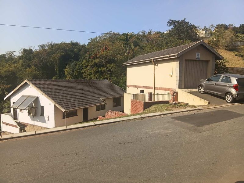 Exterior view of the property featuring a detached garage, tiled roof, and solar water heating system, situated on a sloped residential street.